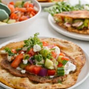 Plate with Greek smashed turkey burger pitas filled with veggies, parsley, feta and sauce.