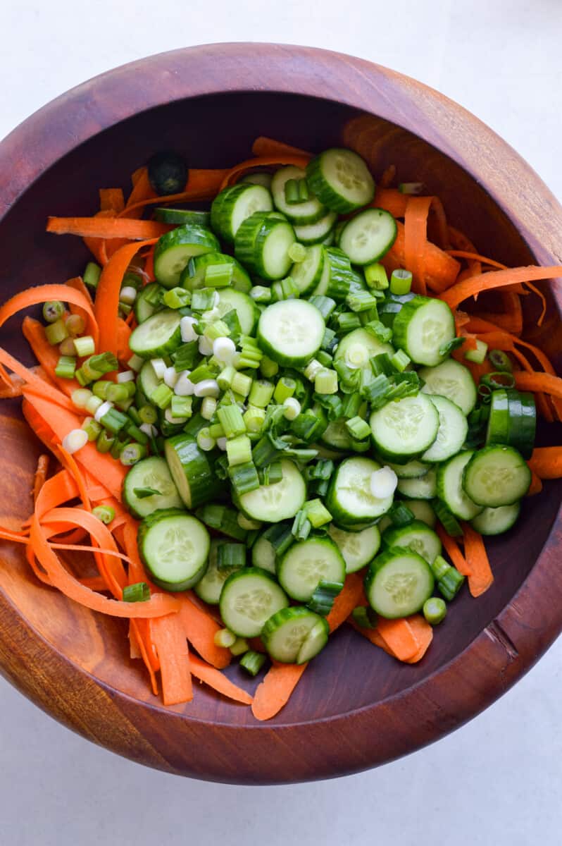 Mixing cucumber coins and shredded carrot ribbons in a bowl.