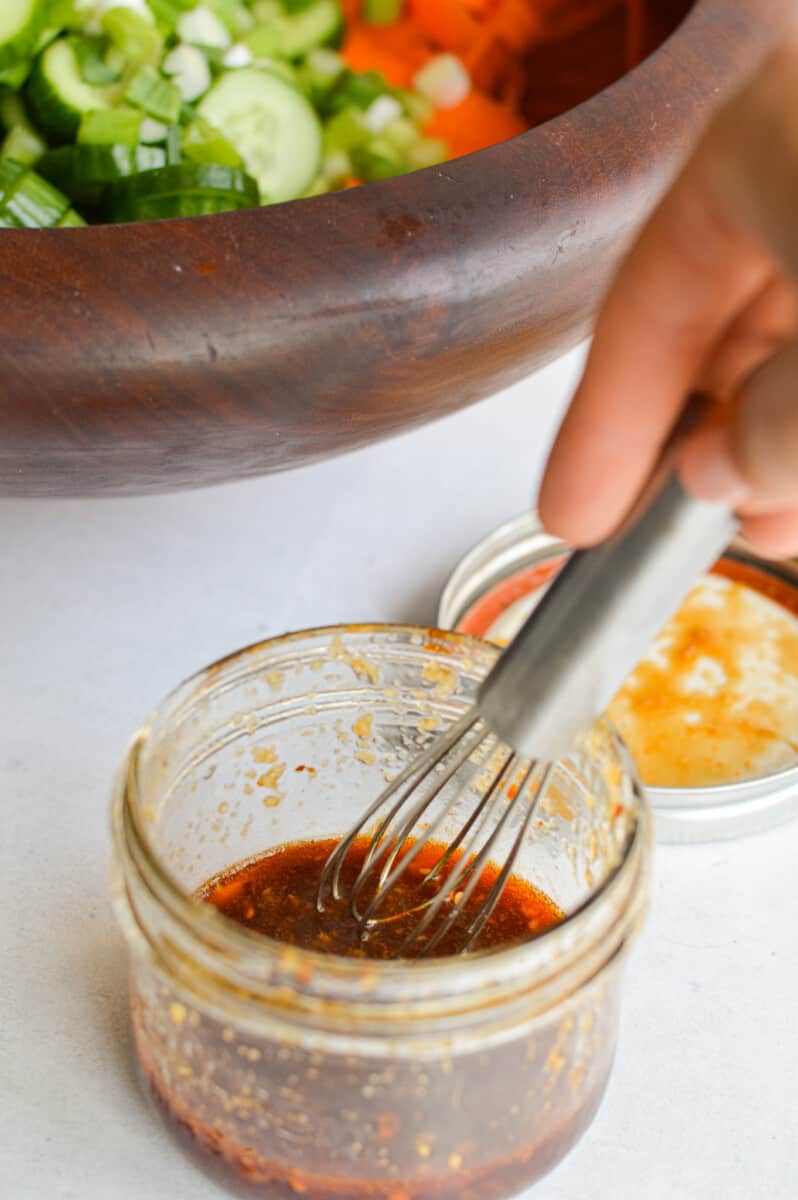 Whisking a salad dressing together with soy sauce, rice vinegar, ginger paste, garlic, honey and chili oil.
