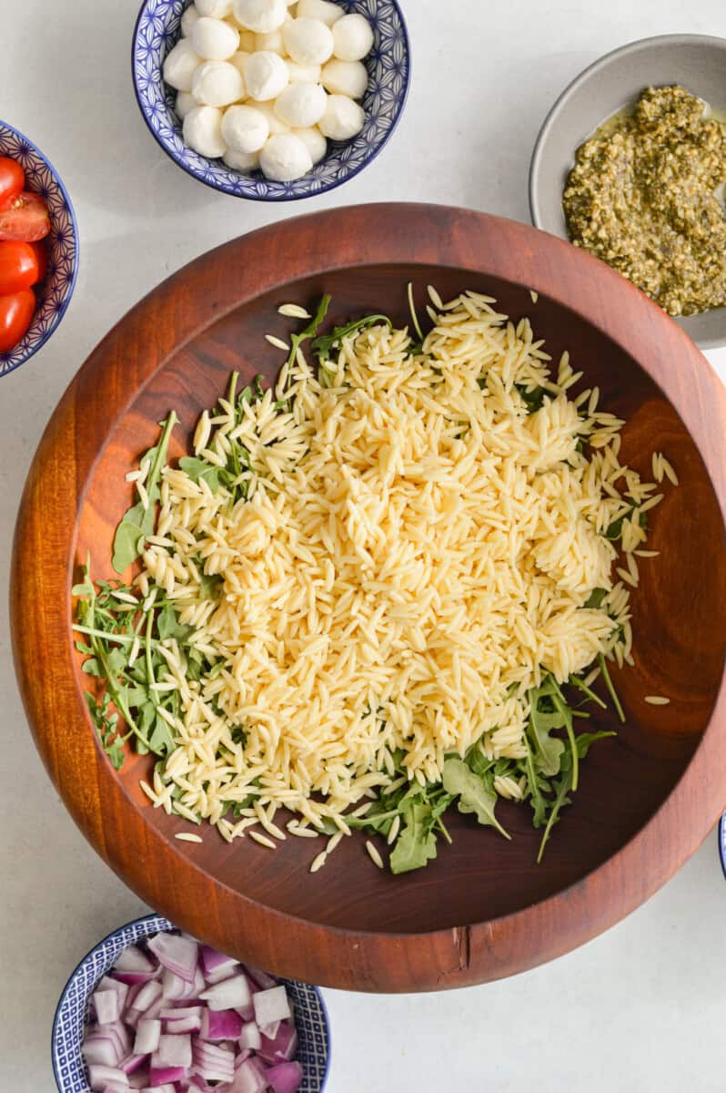 Cooked orzo and arugula in a wooden bowl.