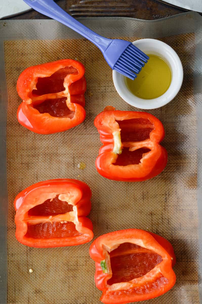 Brushing halved bell peppers with olive oil to roast.