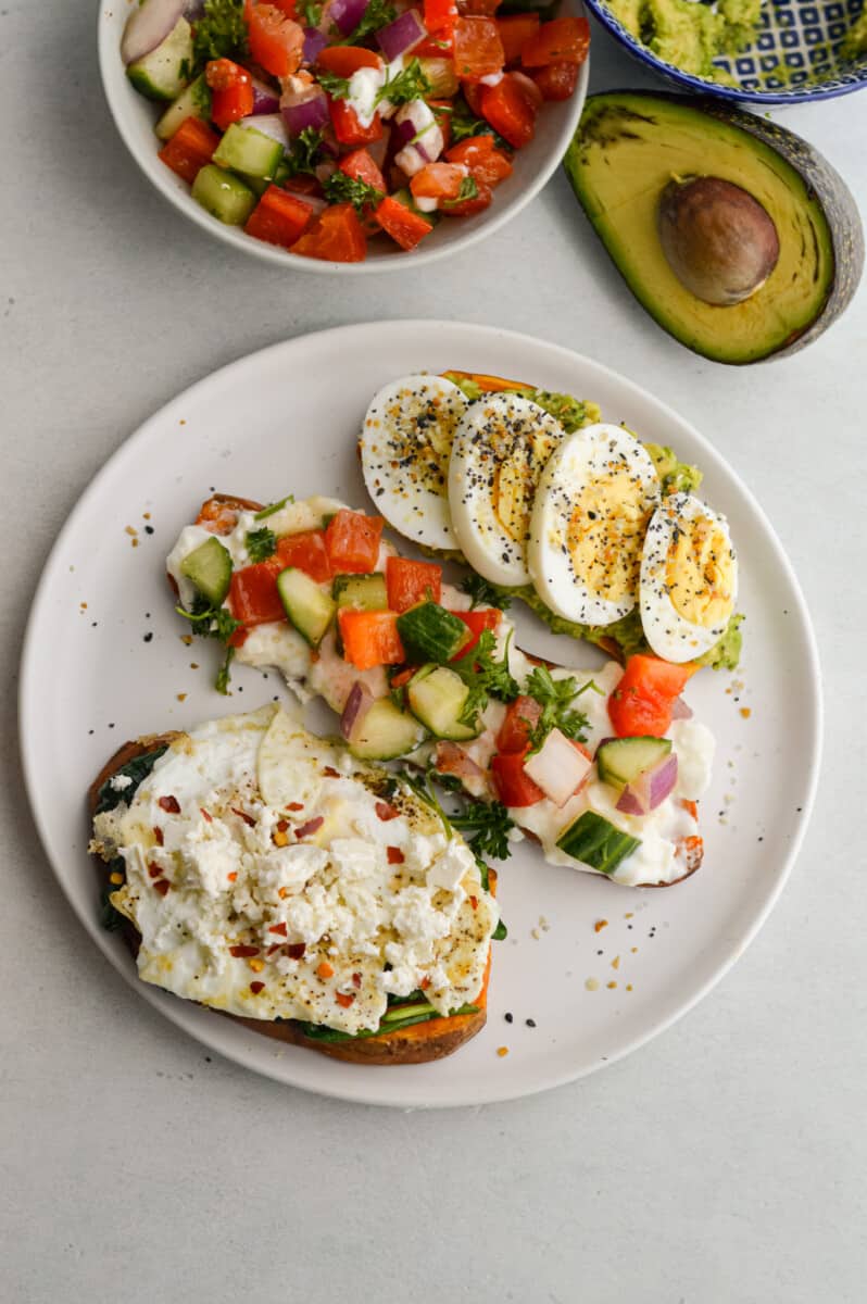 Plate of three sweet potato toasts with avocado egg, veggies and spinach egg whites.