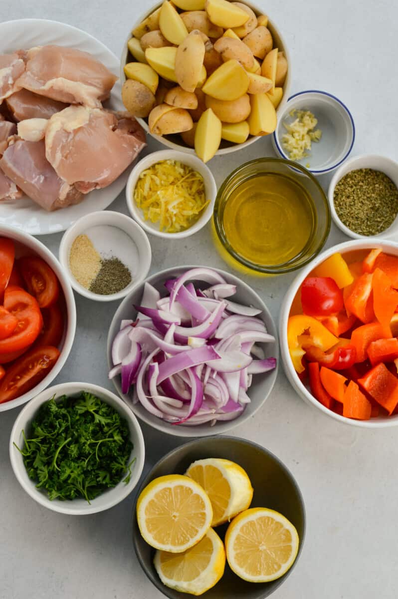 Ingredients including red onion, bell pepper, parsley, chicken thighs, olive oil, feta cheese, spices, garlic and lemon.
