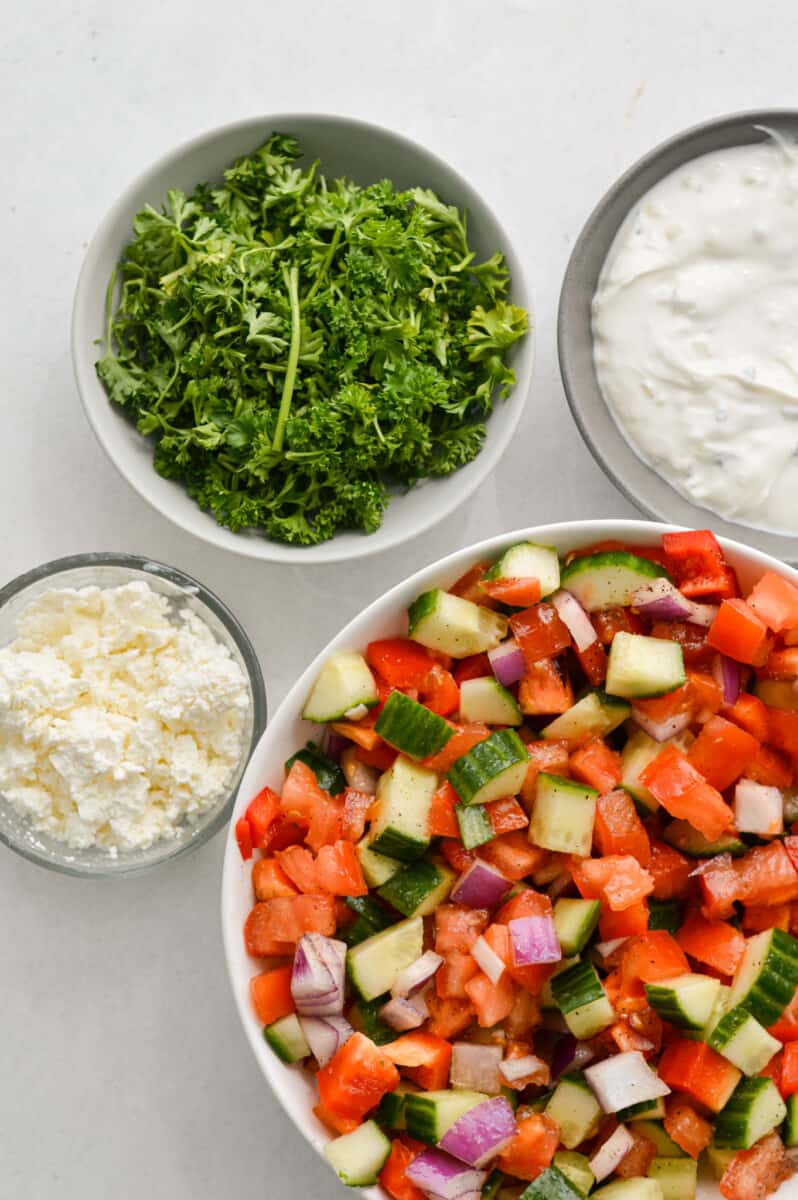Toppings for turkey pita including chopped cucumbers and tomatoes, parsley, tzatziki and feta cheese.