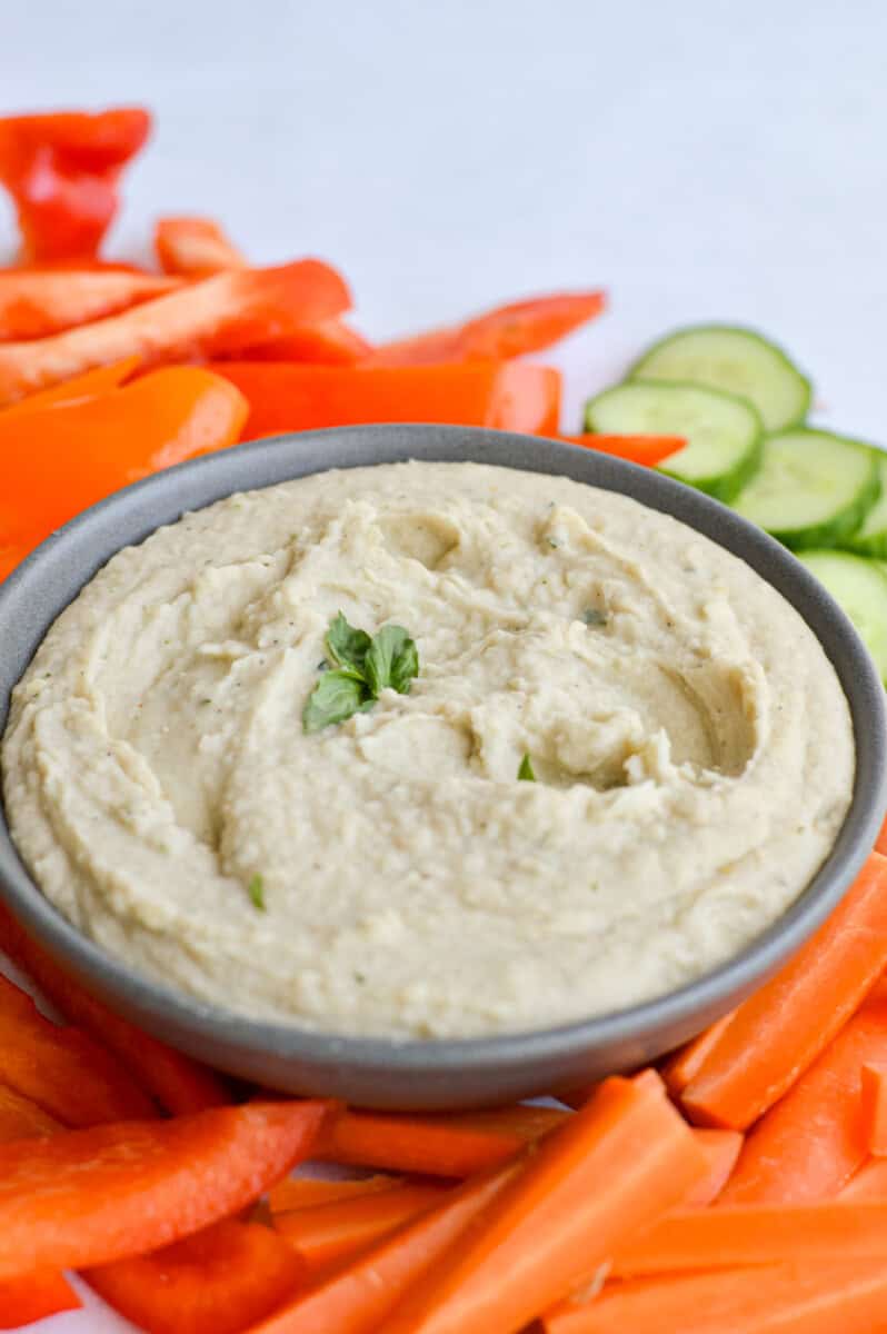Bowl of white bean dip surrounded by cut vegetables.