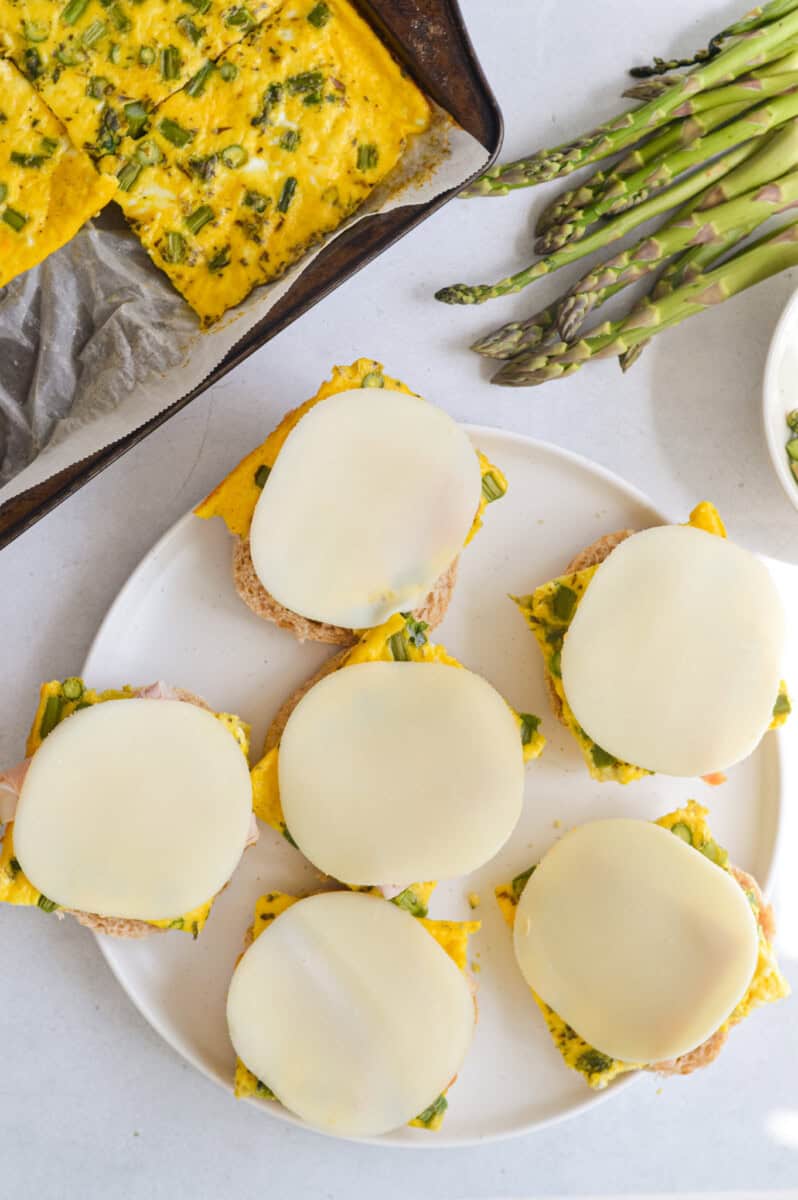 Assembling sheet pan egg sandwiches with cheese and meat.