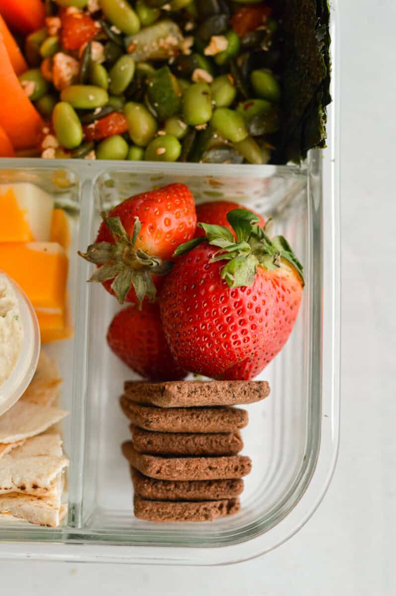 Adding strawberries and chocolate graham crackers to bento box.