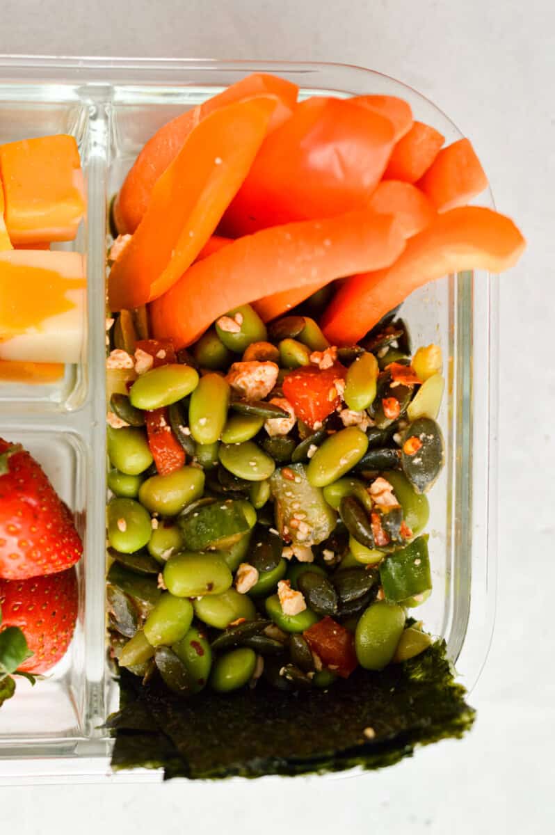 Adding cucumber edamame salad to bento box.
