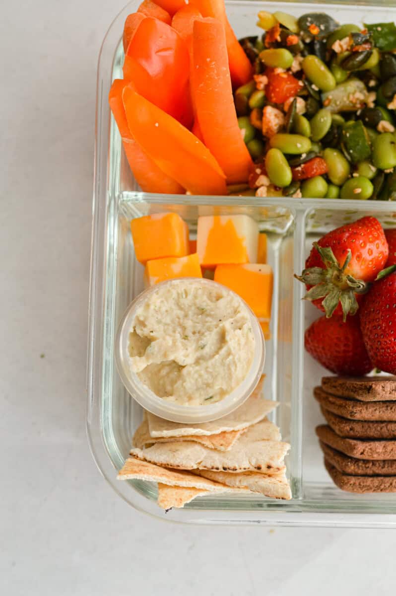 Adding cheese, pita and hummus to bento box.