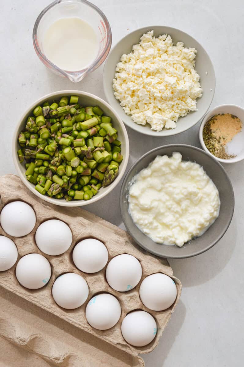 Ingredients including eggs, asparagus, cottage cheese, feta cheese, seasoning, and milk.