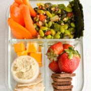 Birds eye of vegetarian bento box with carrots, strawberries, cheese, hummus, pita, cookies and edamame salad.