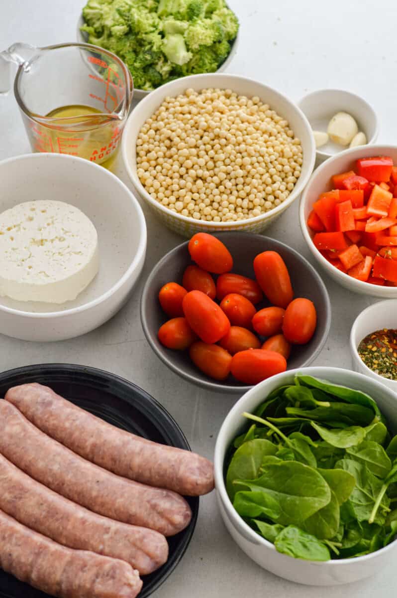 Ingredients including turkey sausage, cherry tomatoes, spinach, red peppers, feta, spices, couscous and oil.