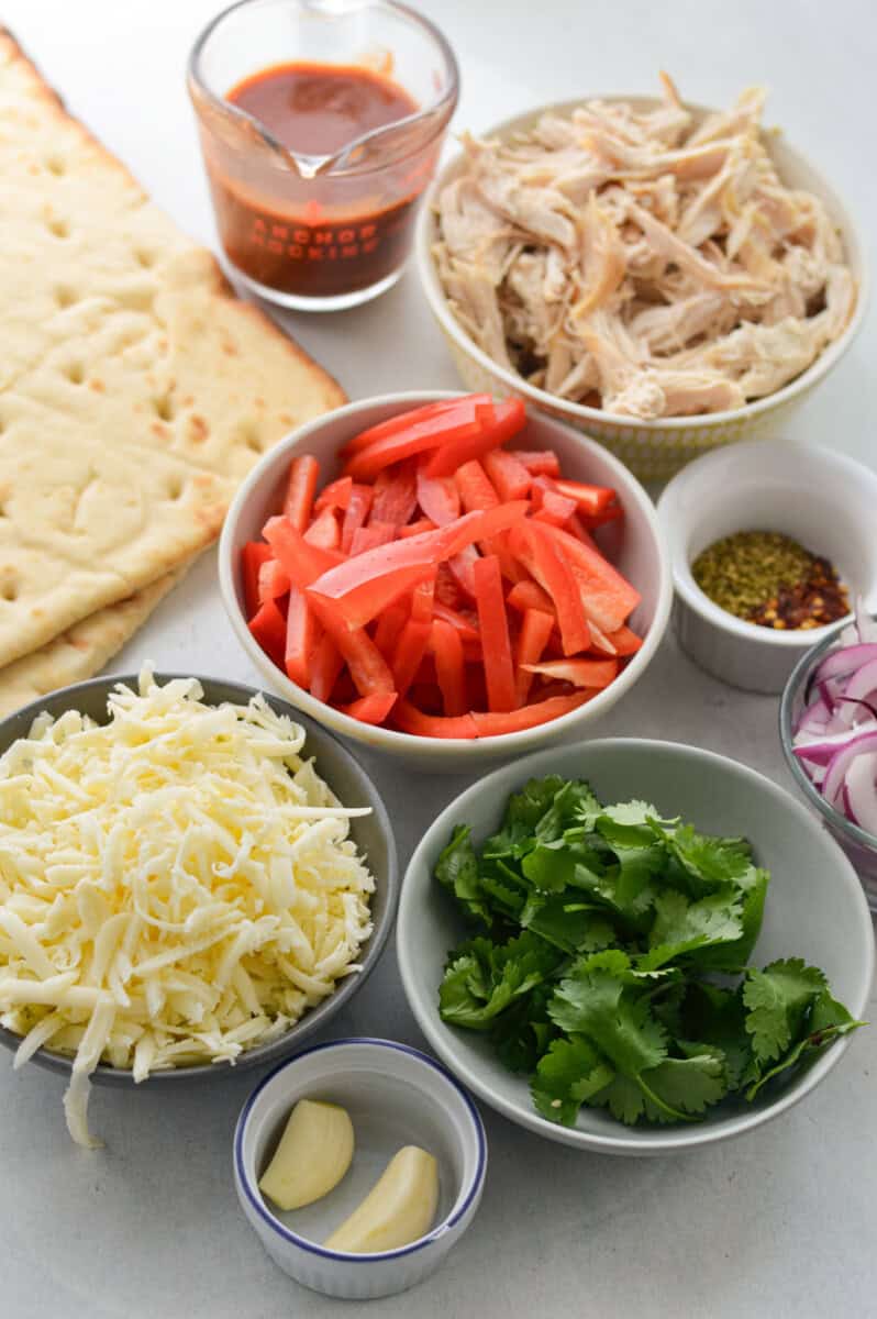 Ingredients like flatbread, bbq sauce, chicken, cilantro, cheese, red pepper, red onion, and olive oil.