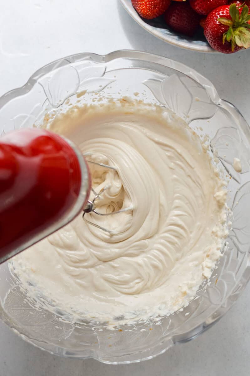 Making cheesecake salad by beating together Greek yogurt, cream cheese, vanilla extract and lemon juice.