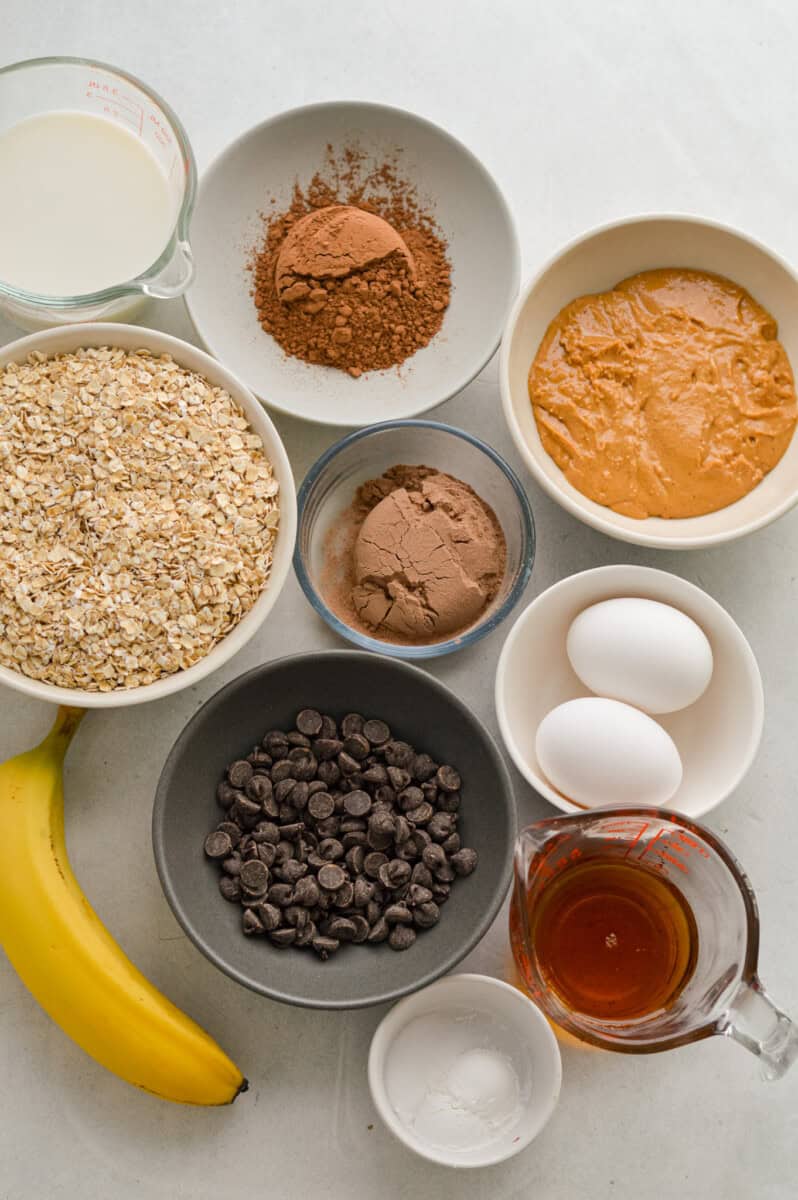 Ingredients including banana, oats, chocolate chips, chocolate protein powder, cocoa powder, eggs, maple syrup, peanut butter.