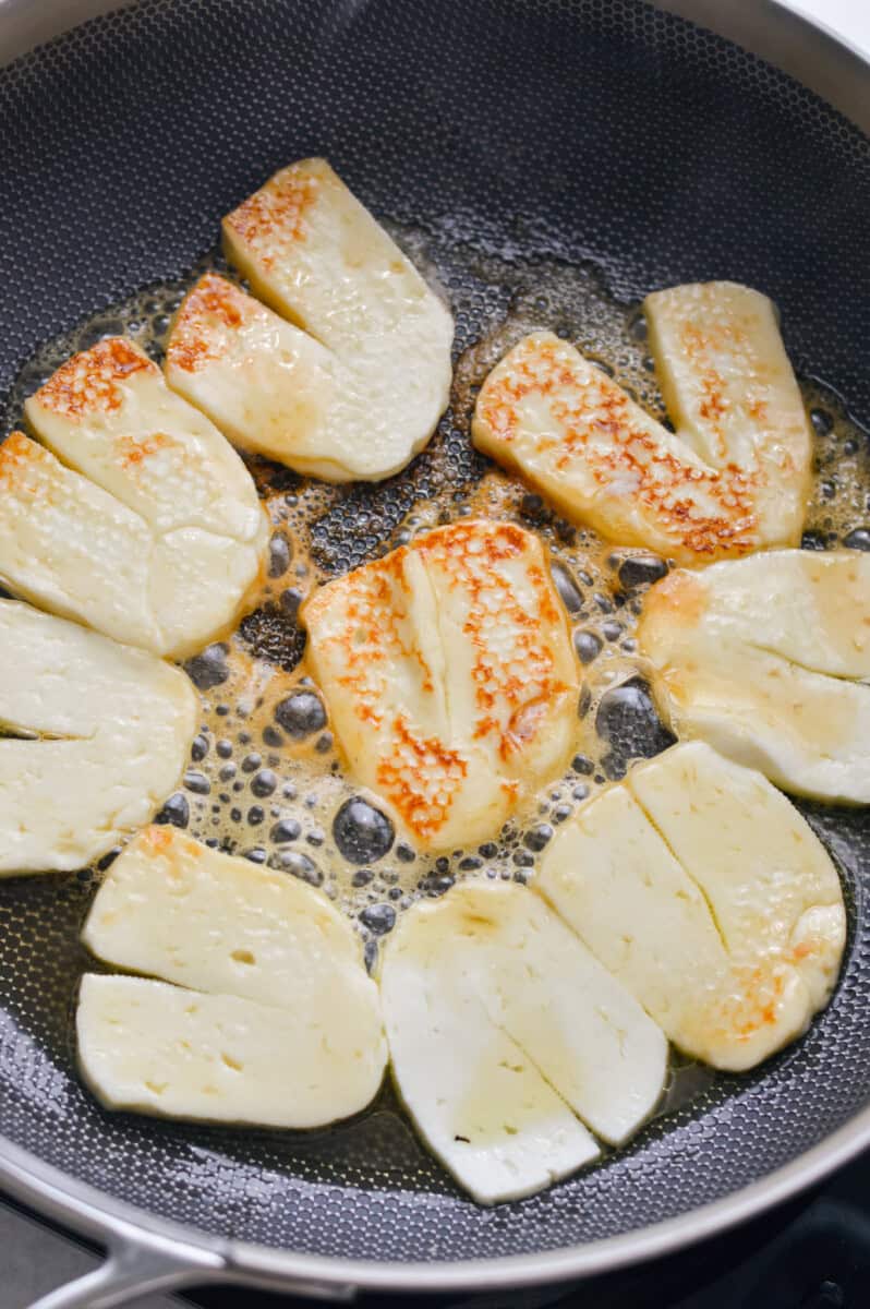 Cooking halloumi in hot honey on a pan.