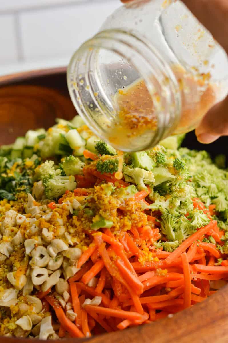 Pouring orange salad dressing on orange quinoa salad.