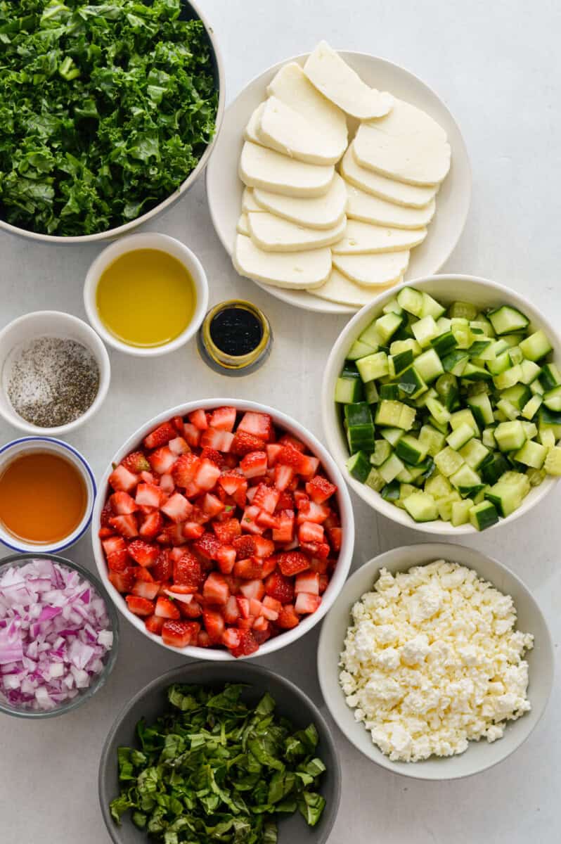 Ingredients including halloumi, cucumber, strawberry, feta cheese, red onion, hot honey, kale, olive oil, balsamic.