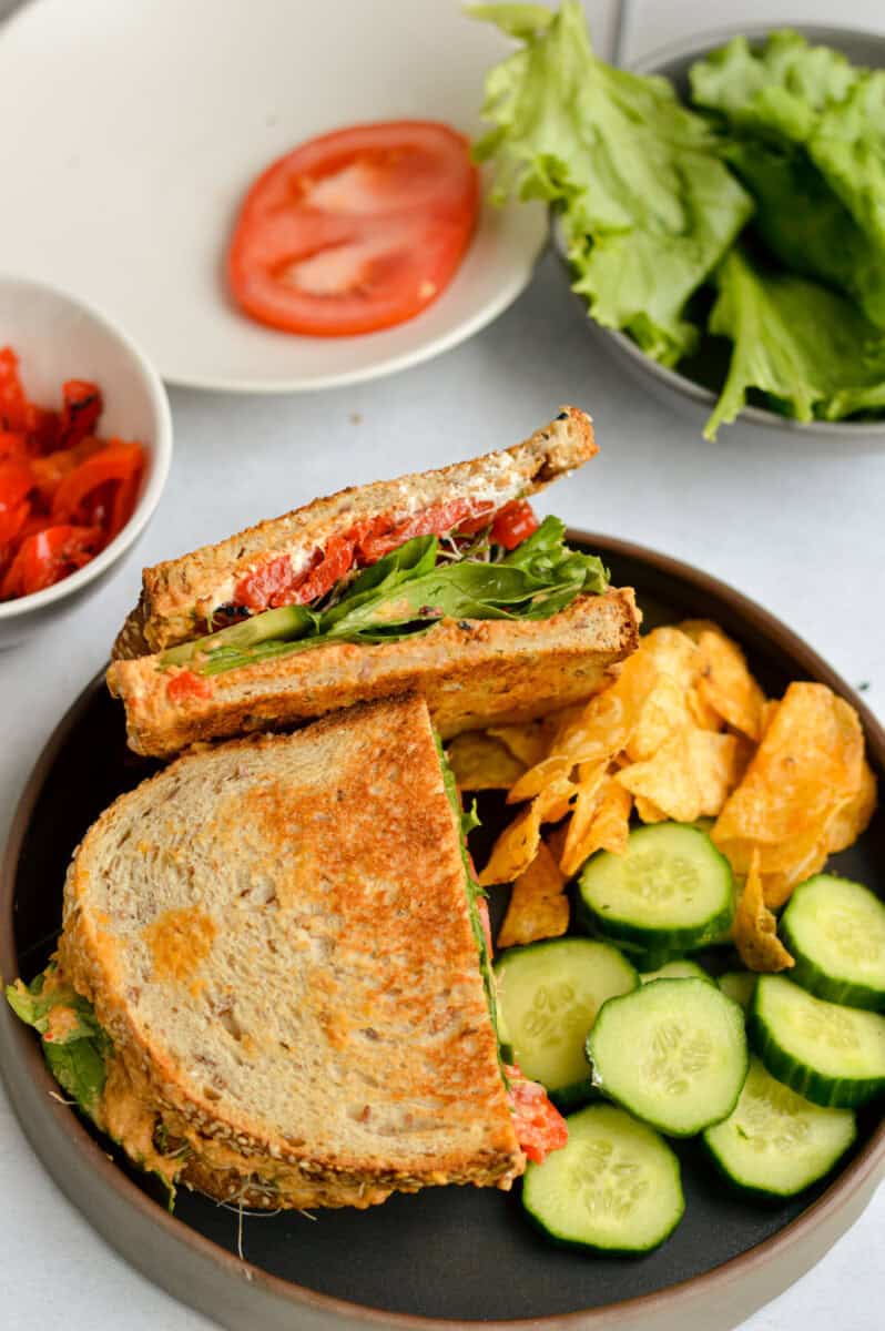 Lunch plate with veggie mediterranean sandwich, cucumber slices and chips.