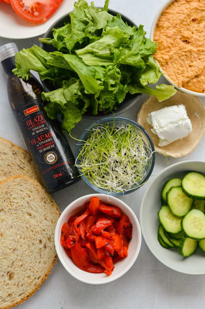 Ingredients including goat cheese, sprouts, cucumber, roasted red peppers, lentil hummus, whole grain bread, balsmic glaze, lettuce.