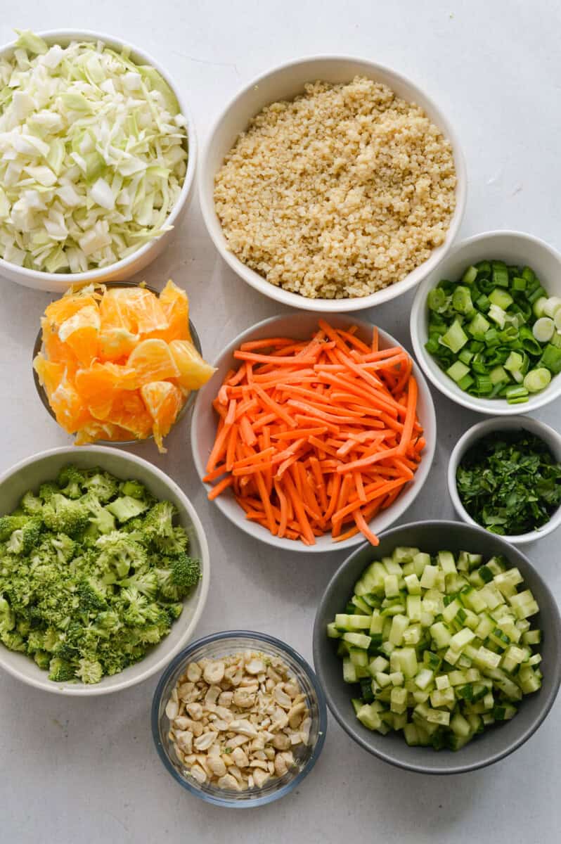 Ingredients including shredded carrot, broccoli, cucumber, quinoa, orange, cashews, cilantro, green onion and cabbage.