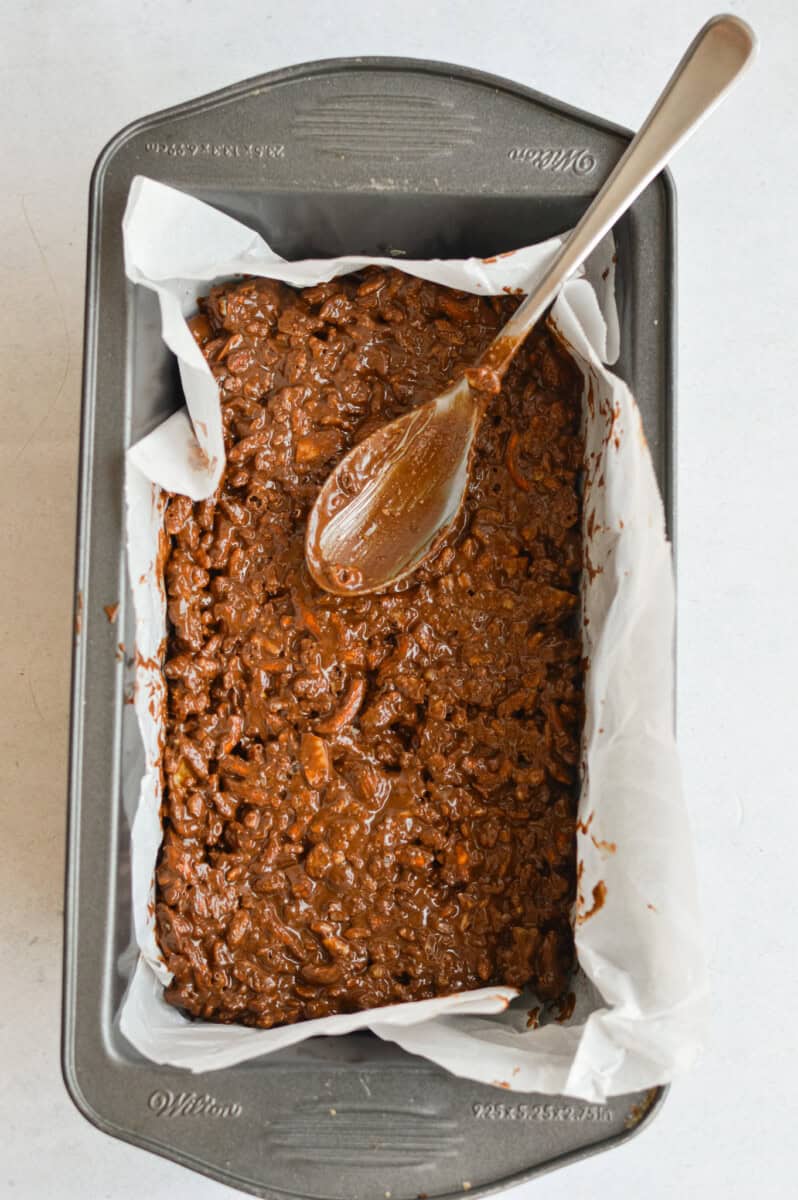Pressing peanut butter crunch bar mixture into a lined loaf pan.