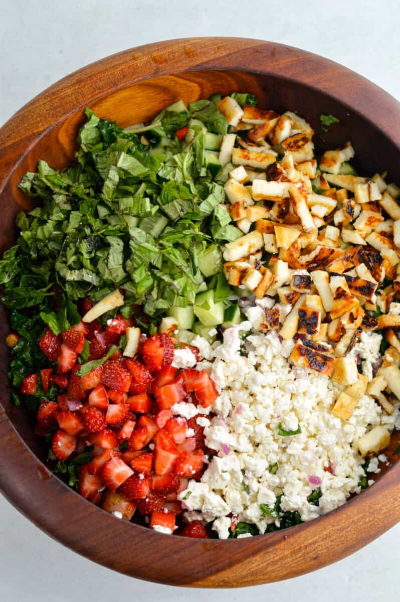 Making a kale salad with cucumber, halloumi, feta, strawberries, onion and basil.