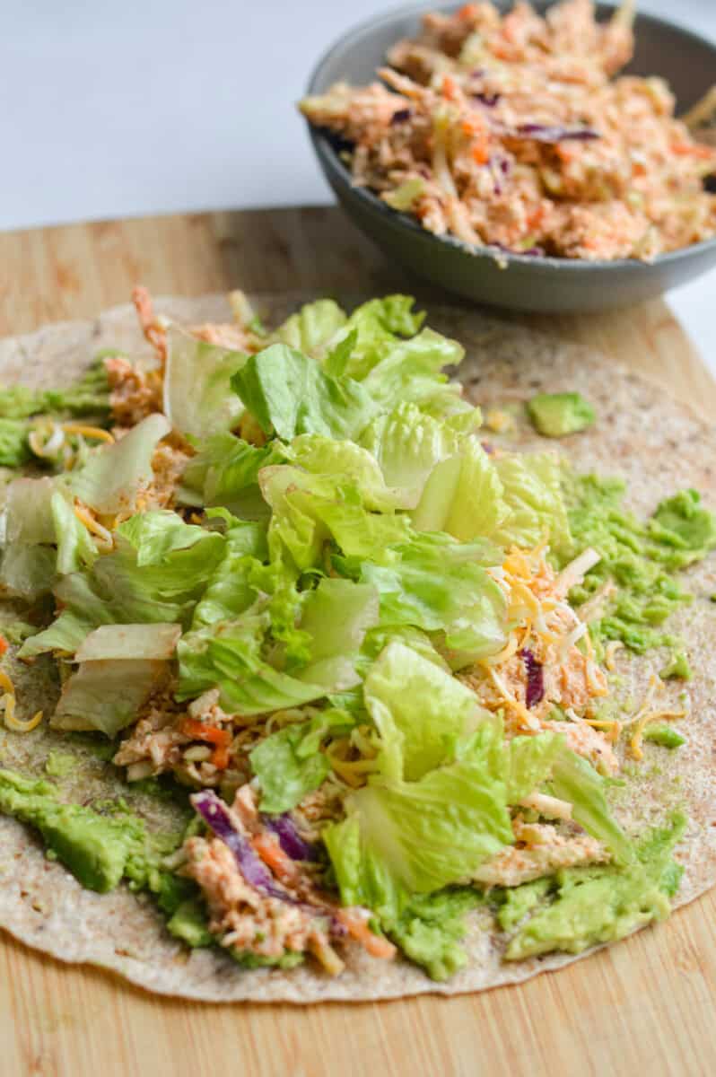 Adding shredded cheese, chicken salad and lettuce to tortilla.