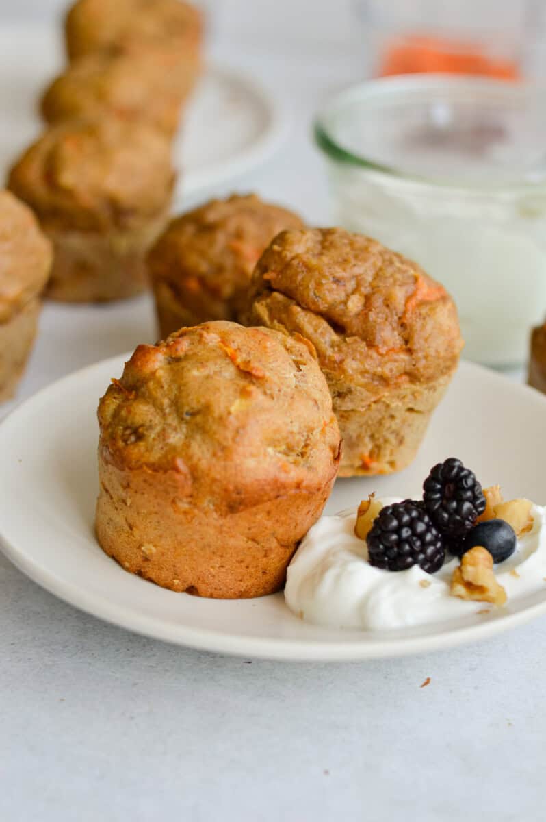 Two healthy breakfast muffins on a plate with yogurt and berries.