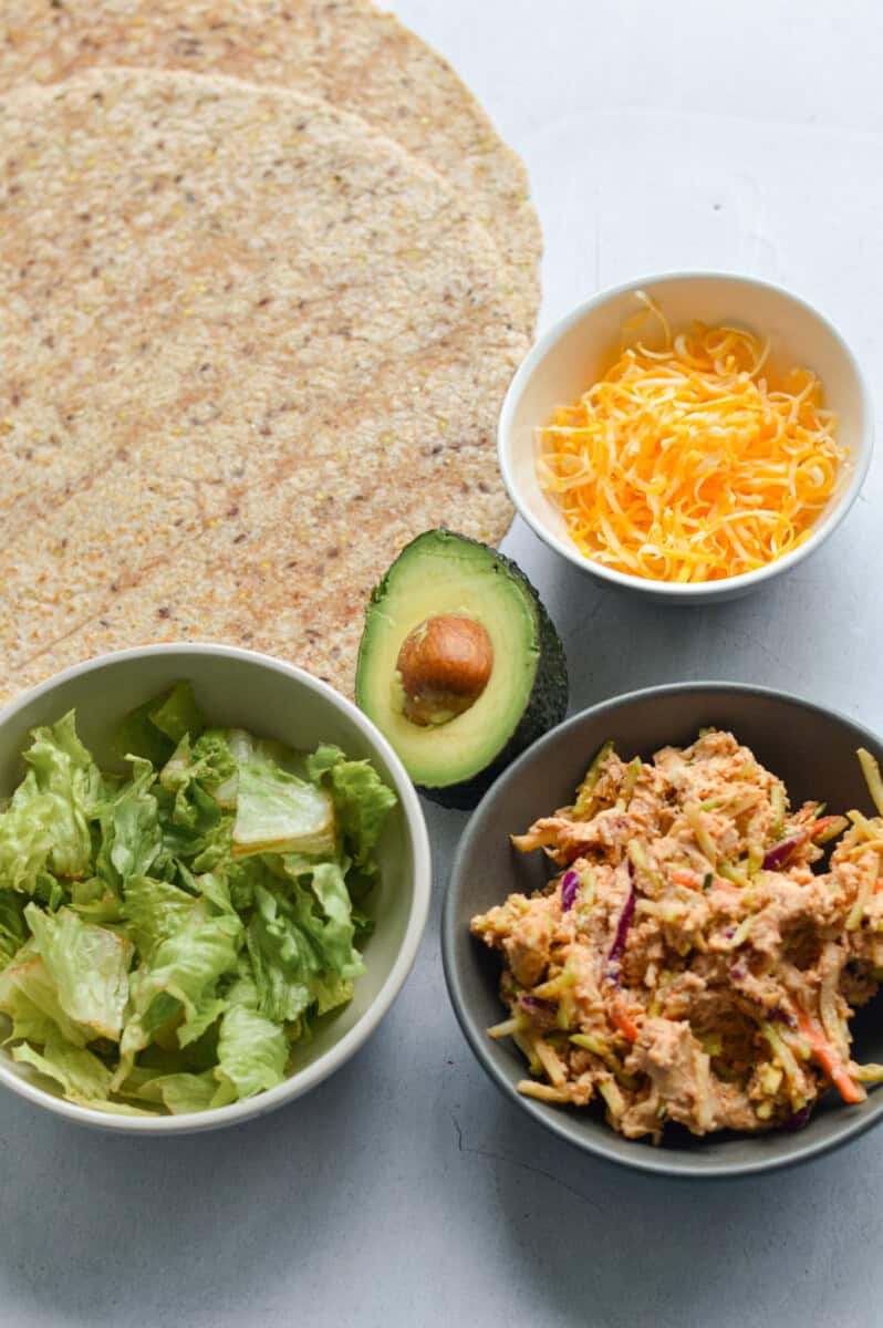 Ingredients including whole wheat tortilla, shredded cheese, chicken salad, avocado and lettuce.