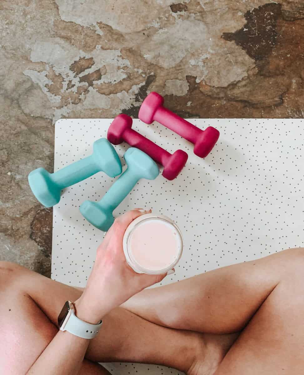Birds eye of a person sitting on a yoga mat with weights and a protein shake.