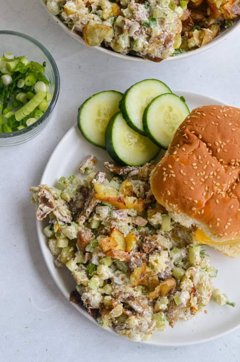 Plate with smashed potato salad, burger bun and cucumber slices.