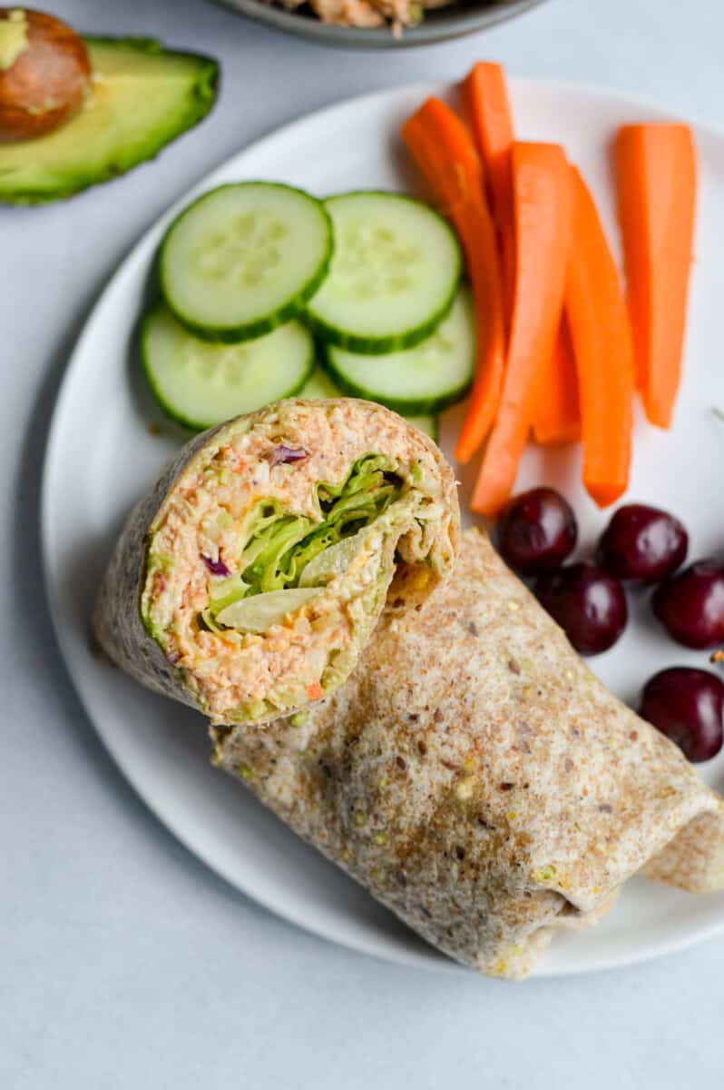 Plate with chicken salad wrap, cucumbers, carrots and grapes.
