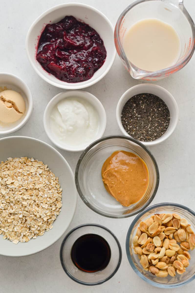 Ingredients including oats, peanut butter, chia jam, greek yogurt, protein powder, milk, berries, and crushed peanuts.