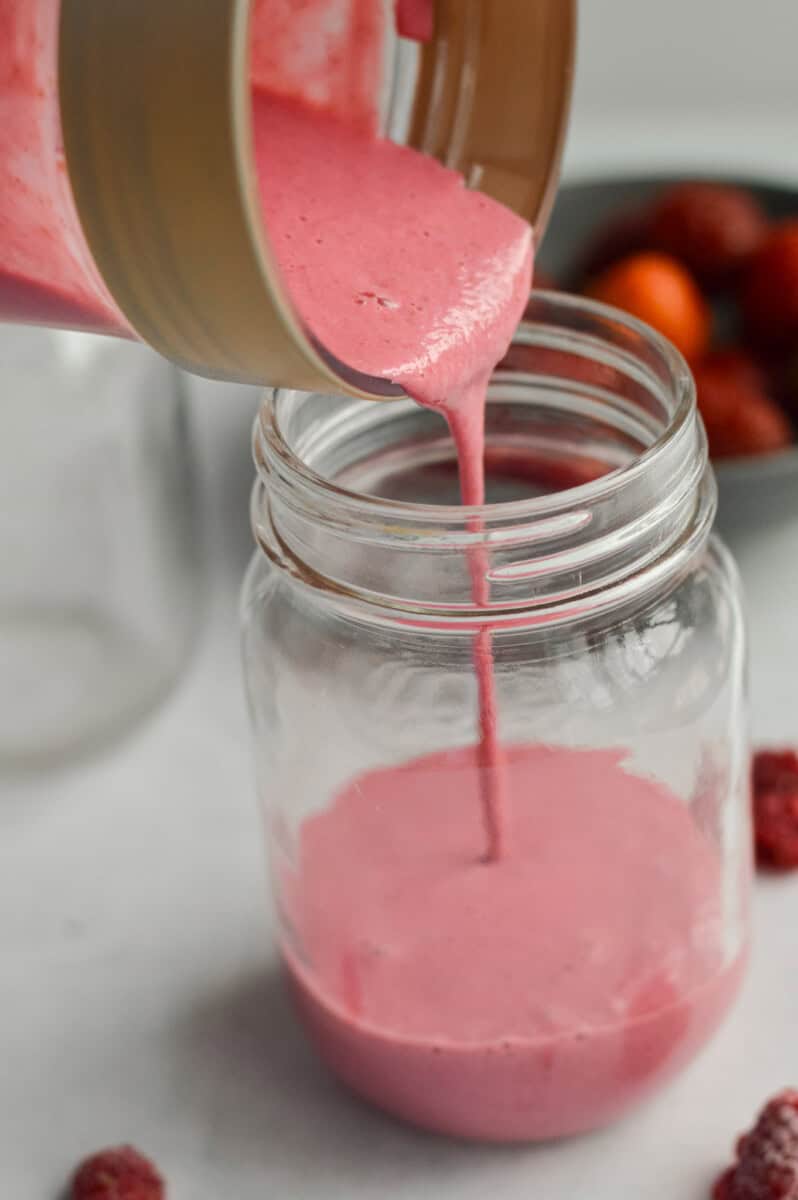 Pouring a pink smoothie into a jar.