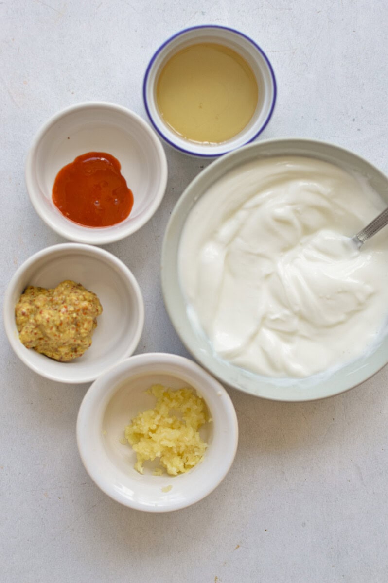 Bowl of Greek yogurt, mayo, garlic, spices, olive oil, white vinegar, and dijon mustard.