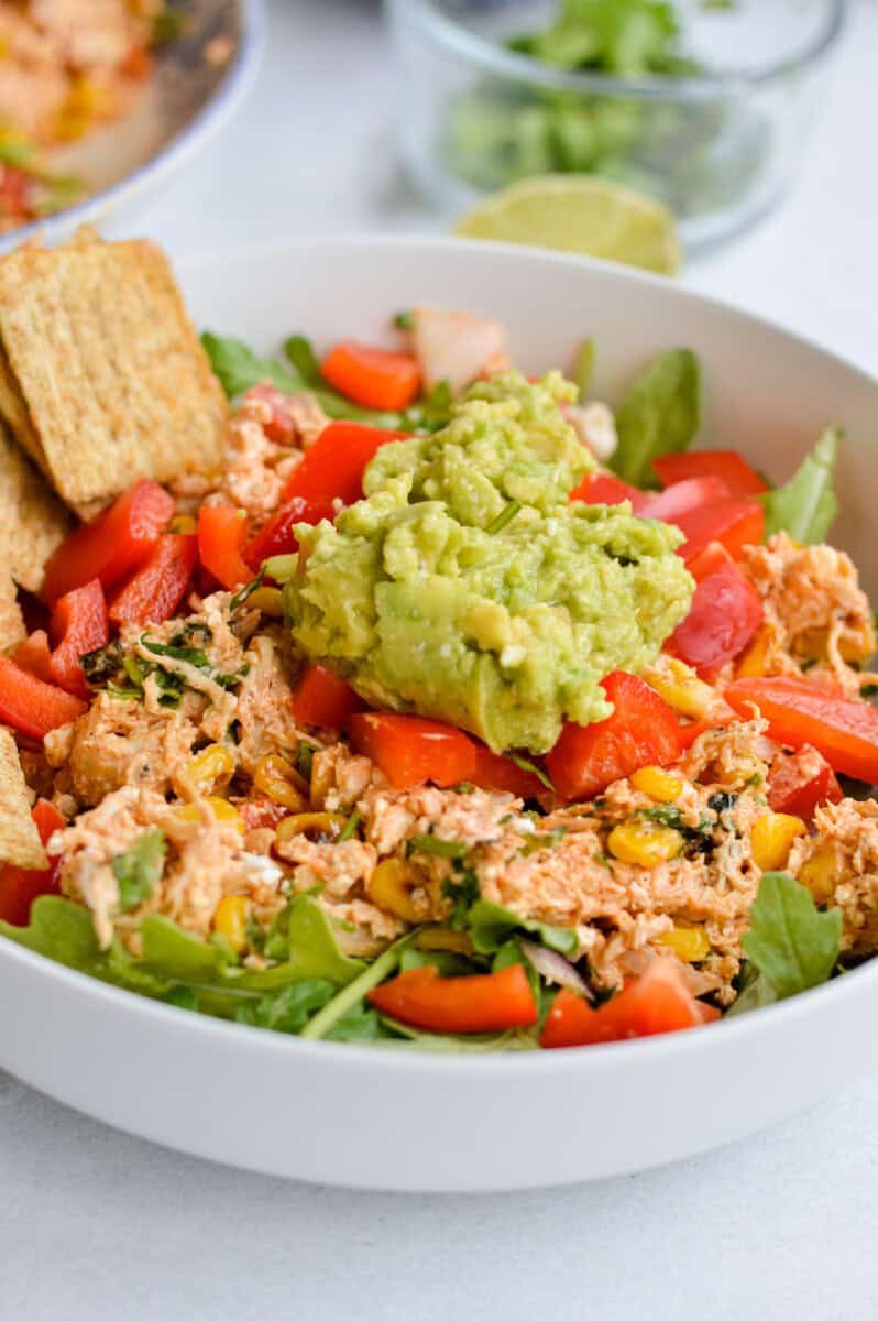A bowl of Mexican chicken salad with guacamole and crackers.