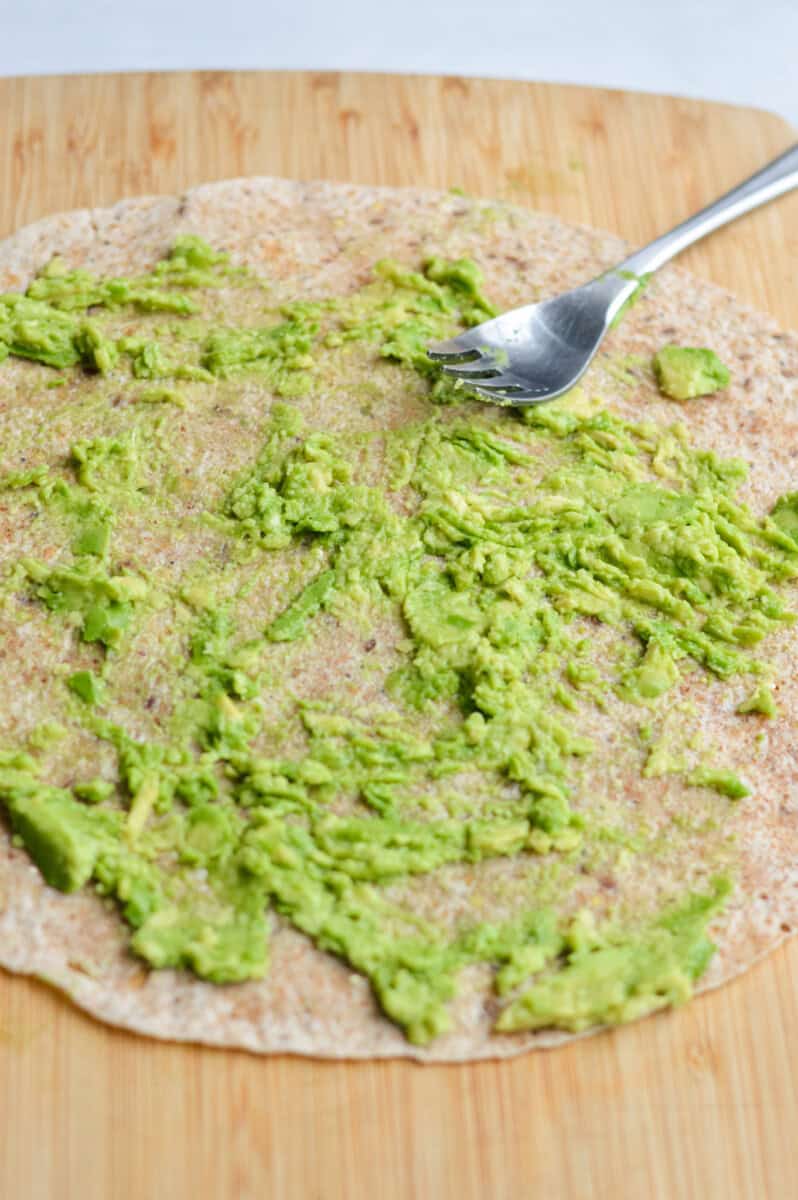 Mashing an avocado onto a whole wheat tortilla.
