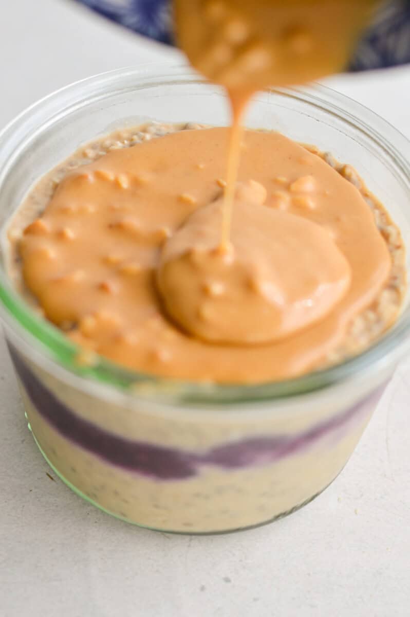 Spreading a layer of peanut butter on top of overnight oats.