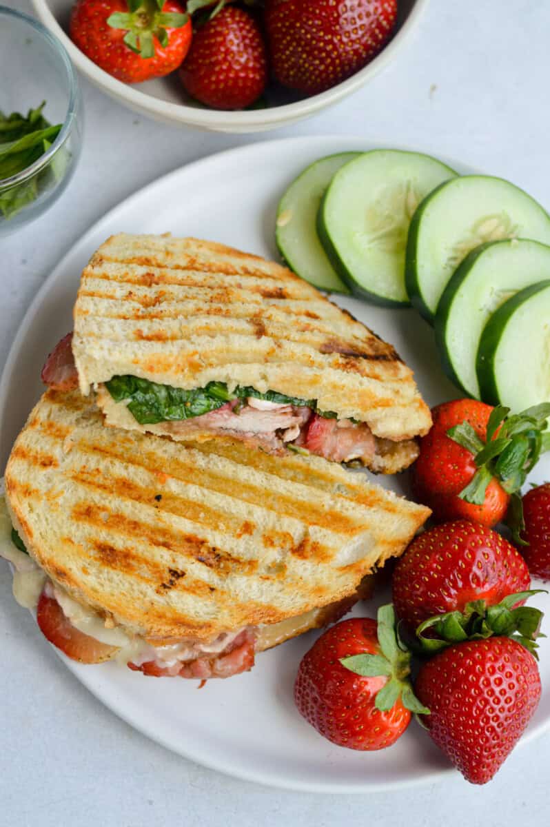 Birds eye of lunch plate with balsamic strawberry and chicken sandwich, served with cucumbers and strawberries.