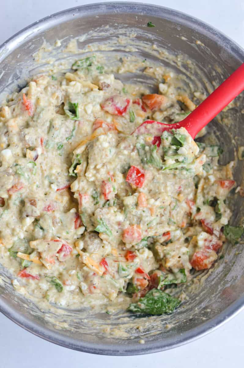 Mixing spinach, cheese and turkey sausage into batter.
