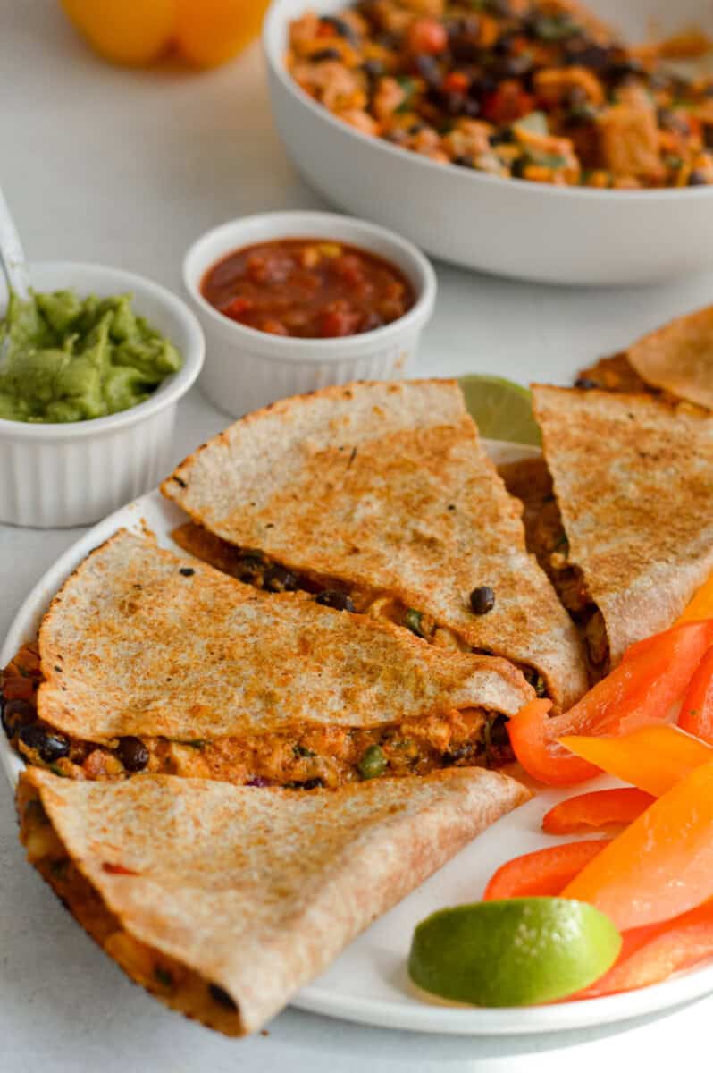 Sliced bbq chicken and black bean quesadilla on a plate with sliced veggies.