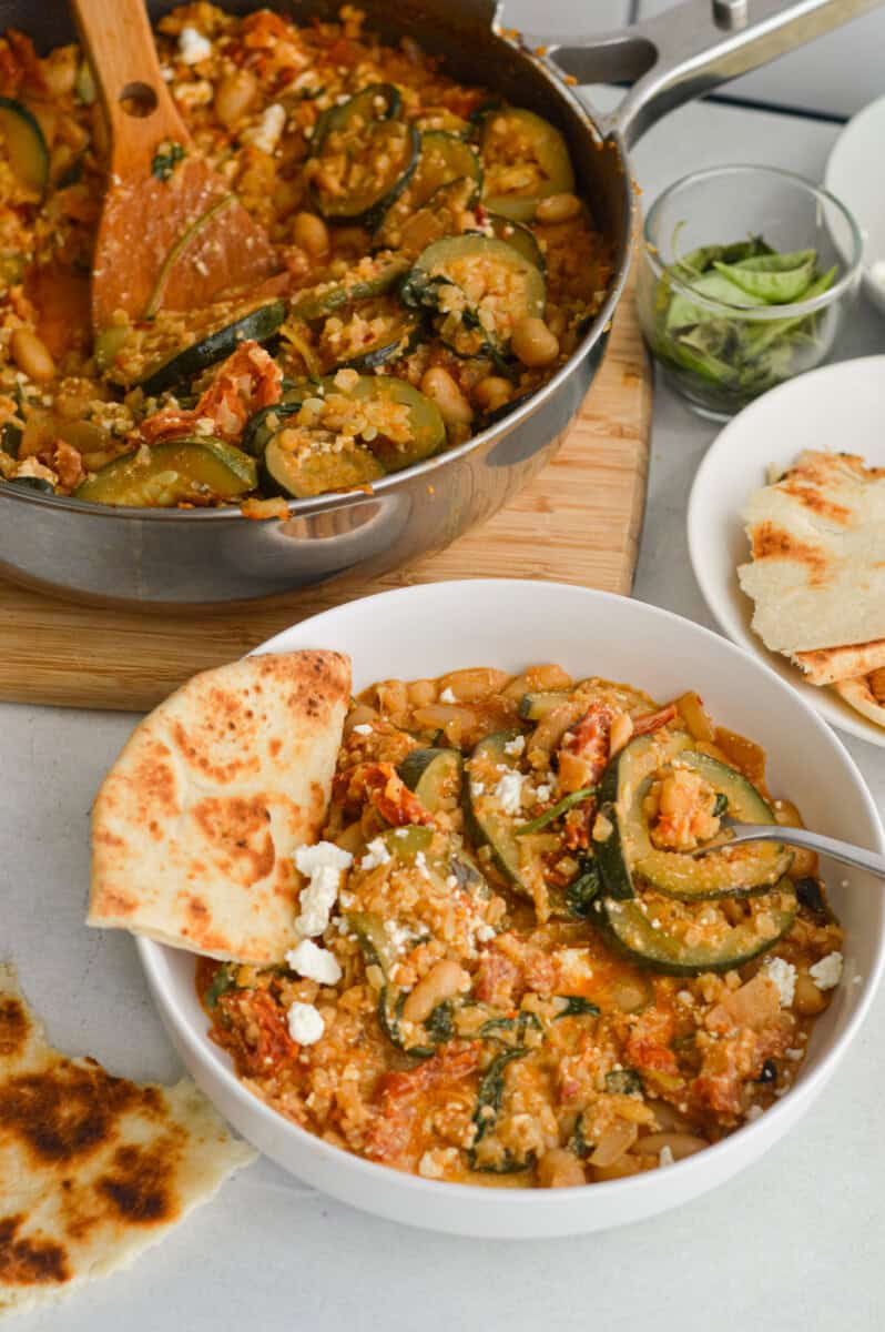 Serving bowls of cheesy white bean tomato bake with pita.