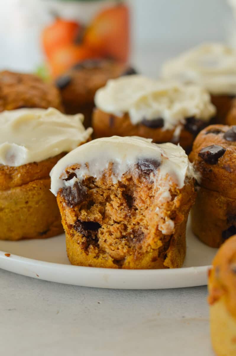 Close up of pumpkin protein muffins with cream cheese frosting. The closest muffin has a bite.