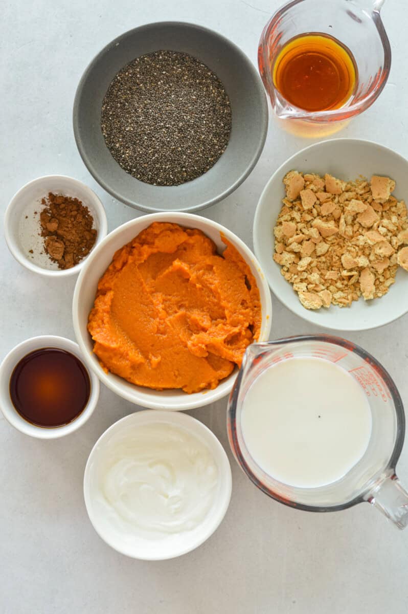 Ingredients including pumpkin puree, graham crackers, milk, greek yogurt, spices, maple syrup, chia seeds and vanilla extract.