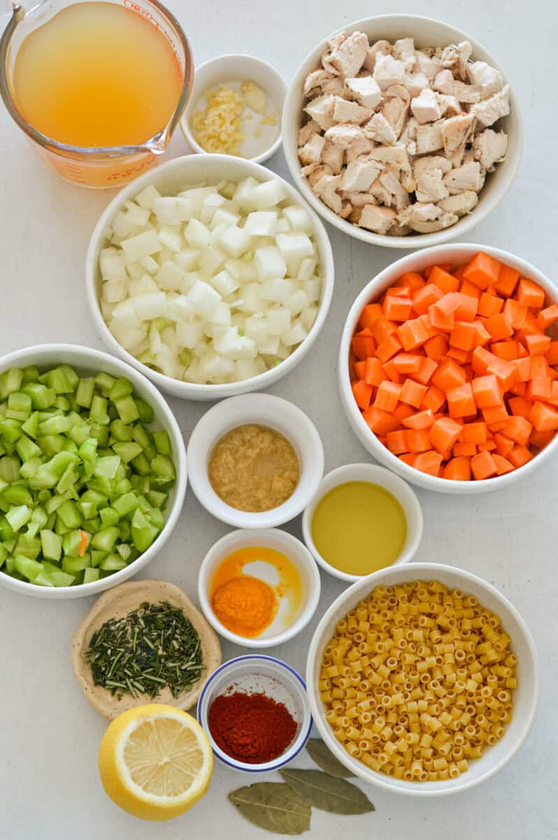 Ingredients including diced onion, celery, carrot, pasta, rotisserie chicken, spices, olive oil, chicken broth, fresh thyme, rosemary and bay leaves.