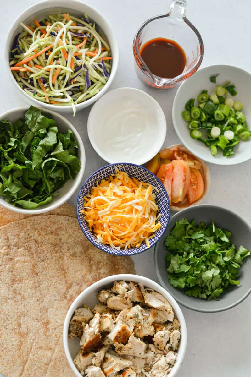 Ingredients including chicken breast, cheese, green onion, bbq sauce, greek yogurt, coleslaw mix, tortilla, spices, tomato and cilantro.