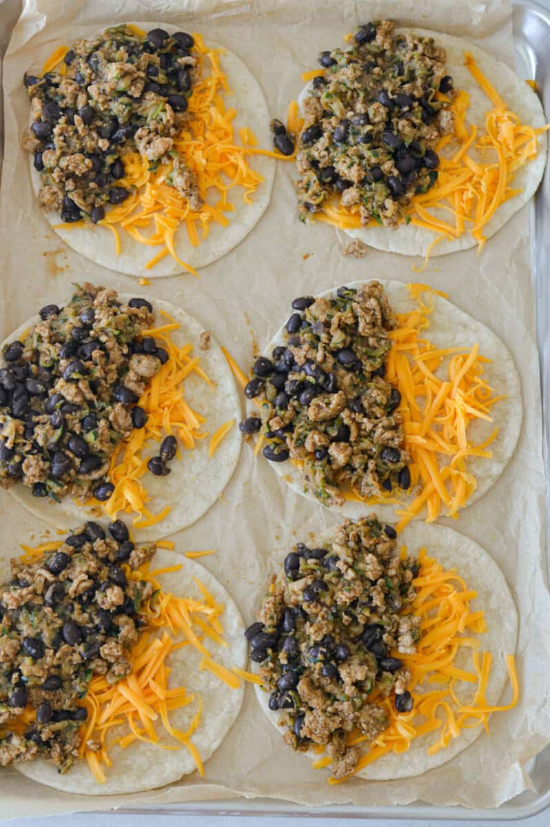 Filling tortillas with shredded cheese and ground chicken filling.