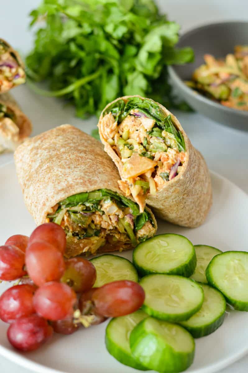 Lunch plate with bbq grilled chicken wrap, cucumber slices and red grapes.