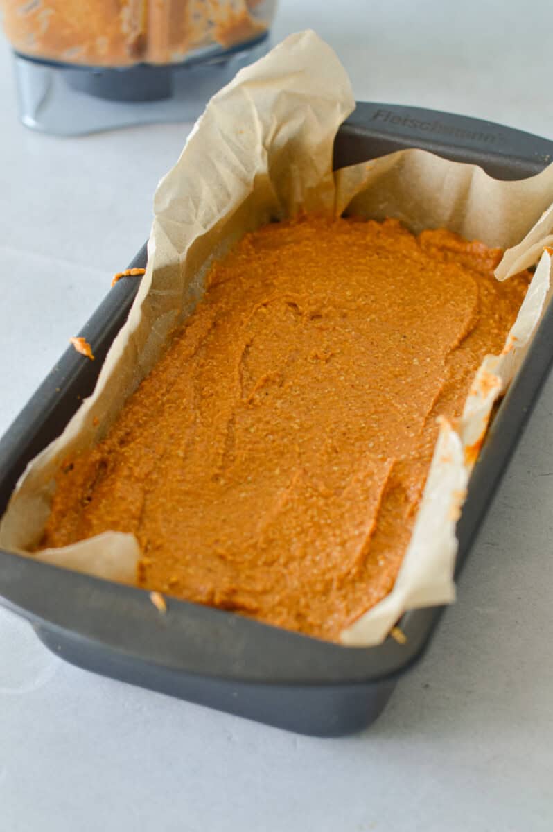 Pouring pumpkin bread batter into a lined loaf pan.